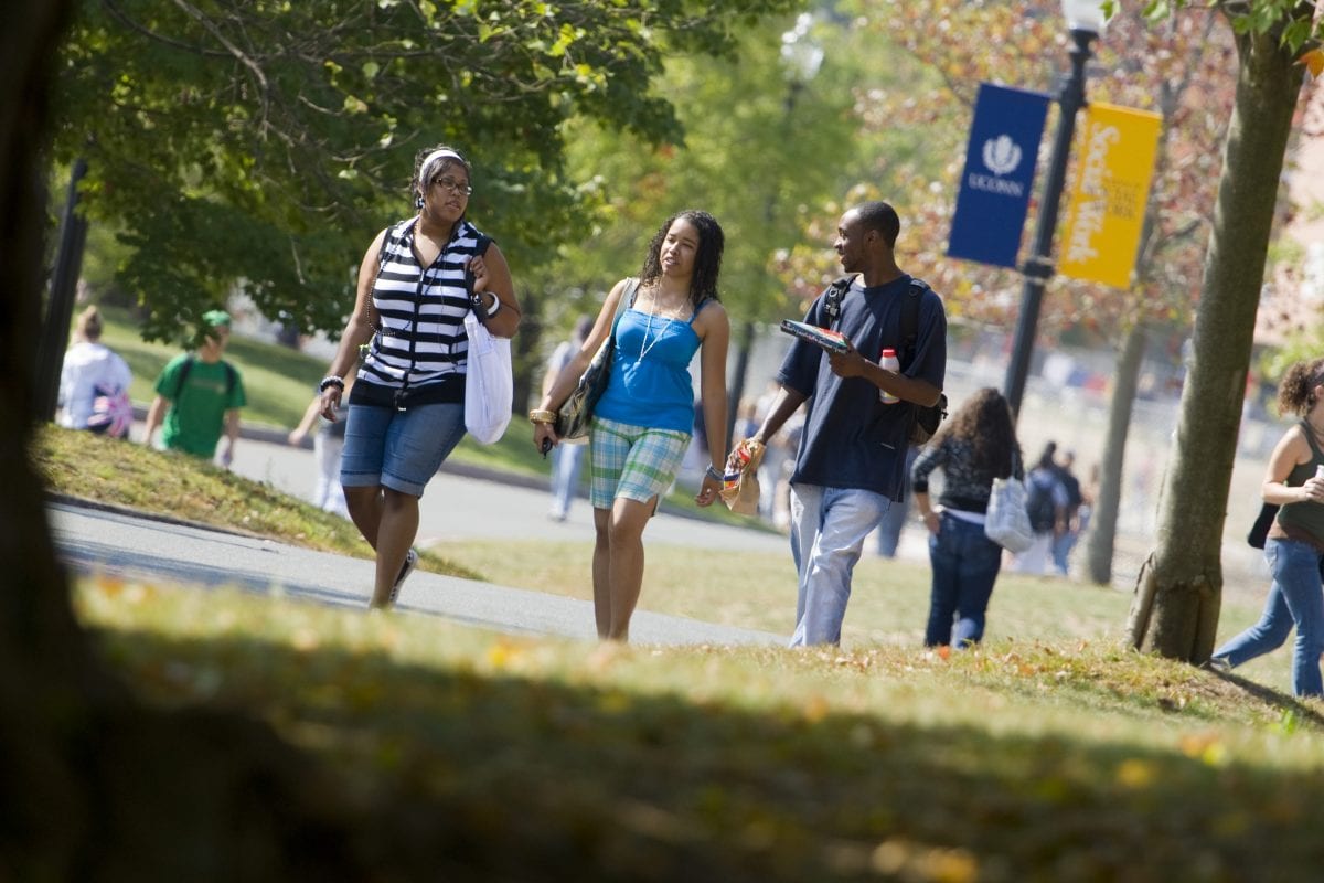 Students walking together on campus under fall foliage near a UConn Student Union banner.