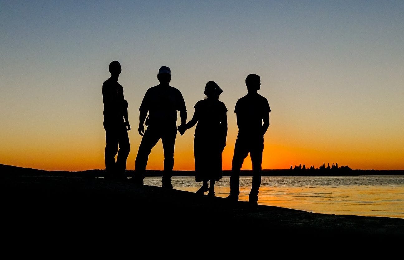 URC Friends of Recovery: Silhouettes of four people standing by the water at sunset, symbolizing friendship, support, and recovery.