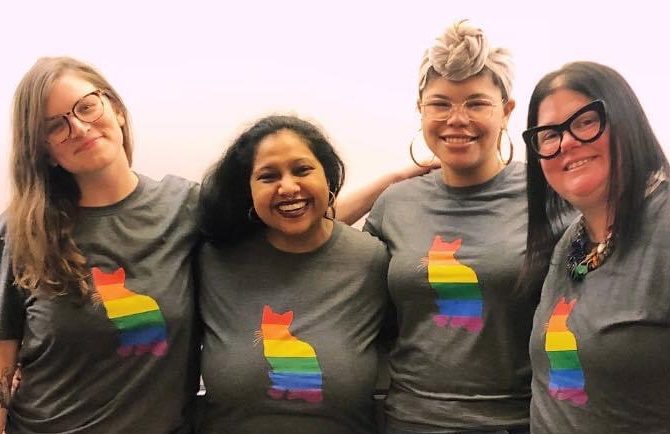 Joleen Nishelli and friends: Four people smiling and posing together, each wearing a gray t-shirt with a rainbow-colored husky logo on the front.