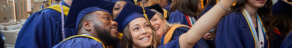 Group of graduates in caps and gowns taking a selfie together, smiling and celebrating.