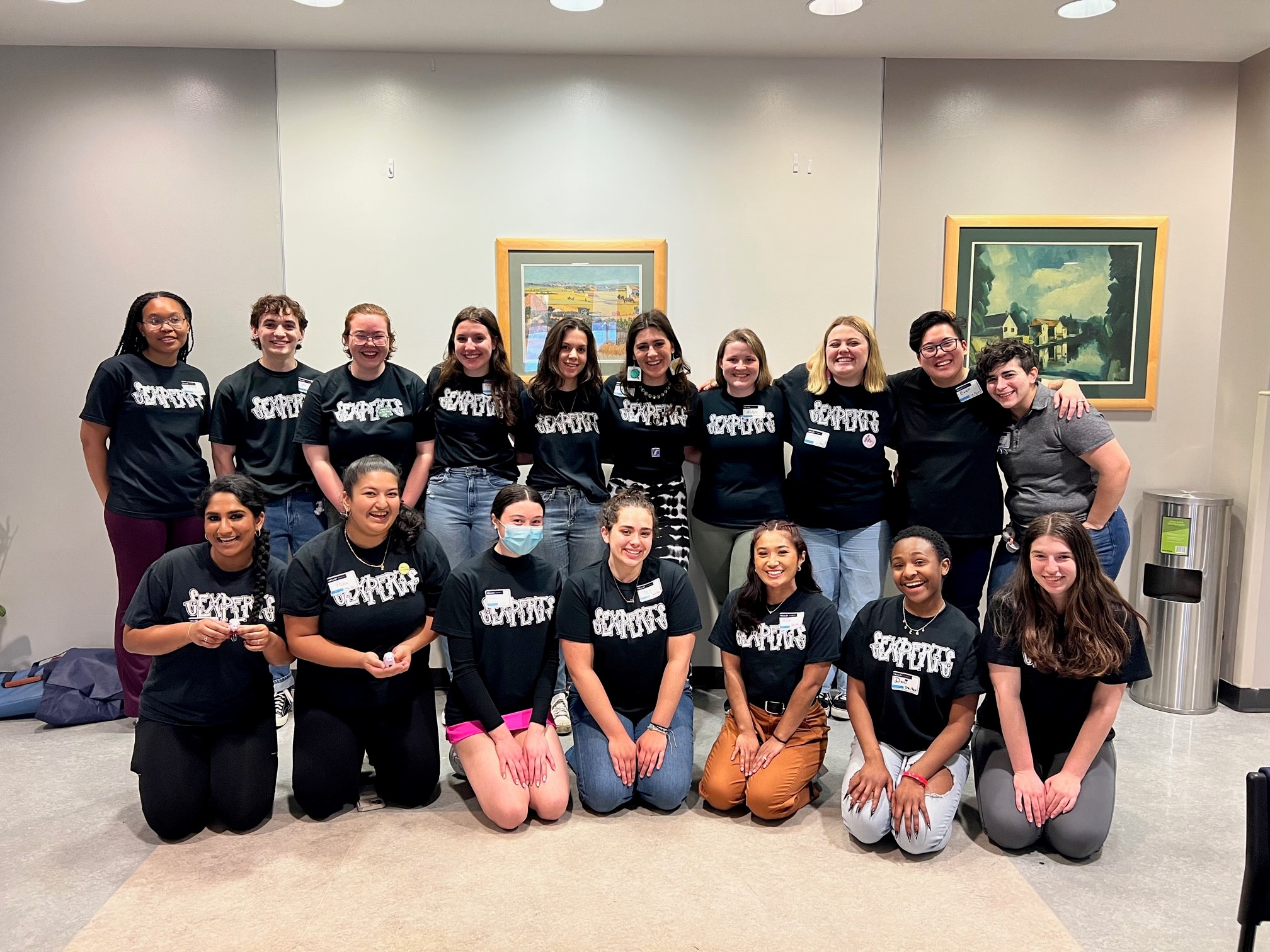 Group photo of Sexperts team members smiling indoors wearing matching black T-shirts with "SEXPERTS" text.