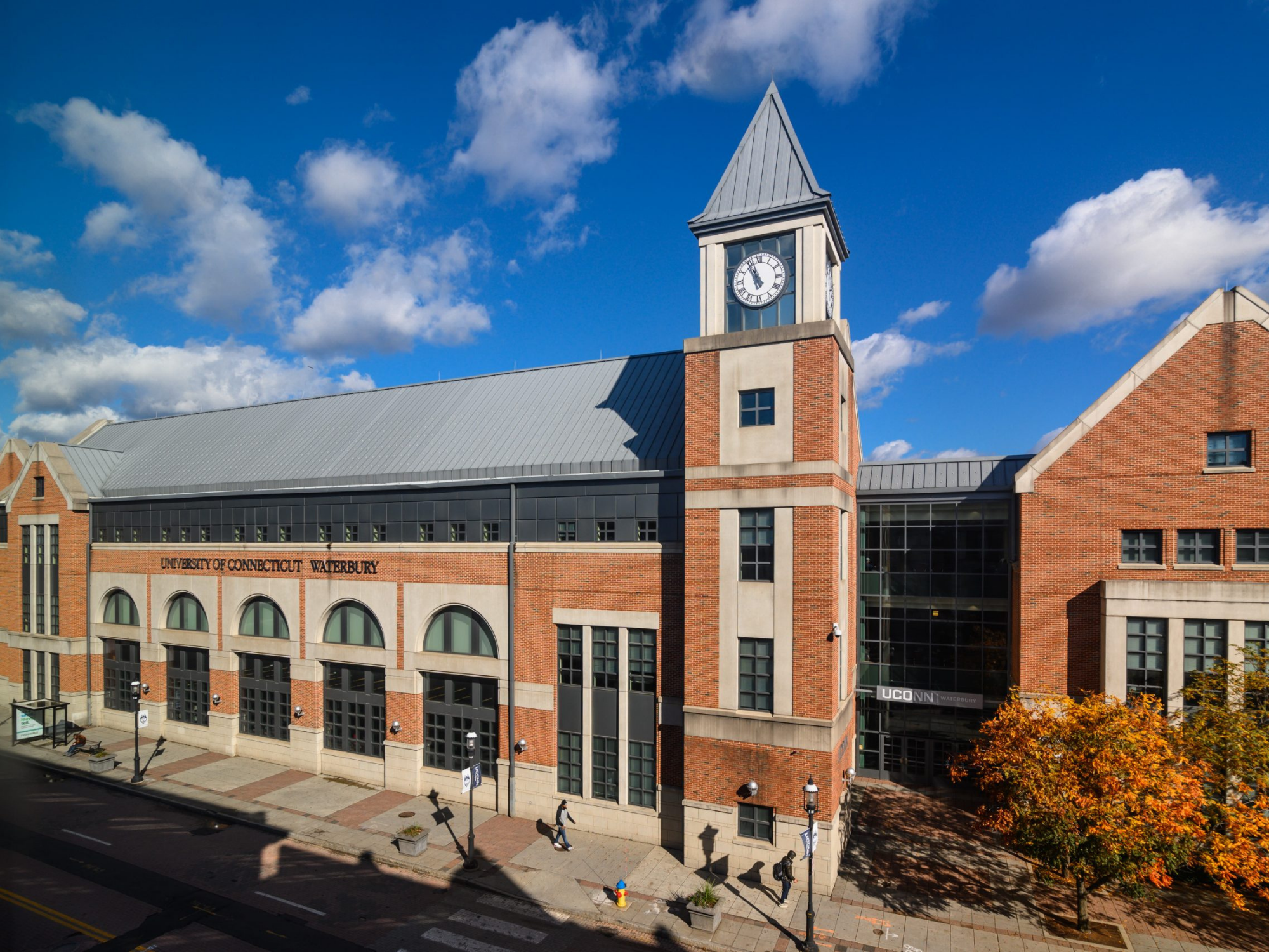 Daytime exterior of UConn Waterbury’s brick campus building with a clock tower and fall foliage nearby.