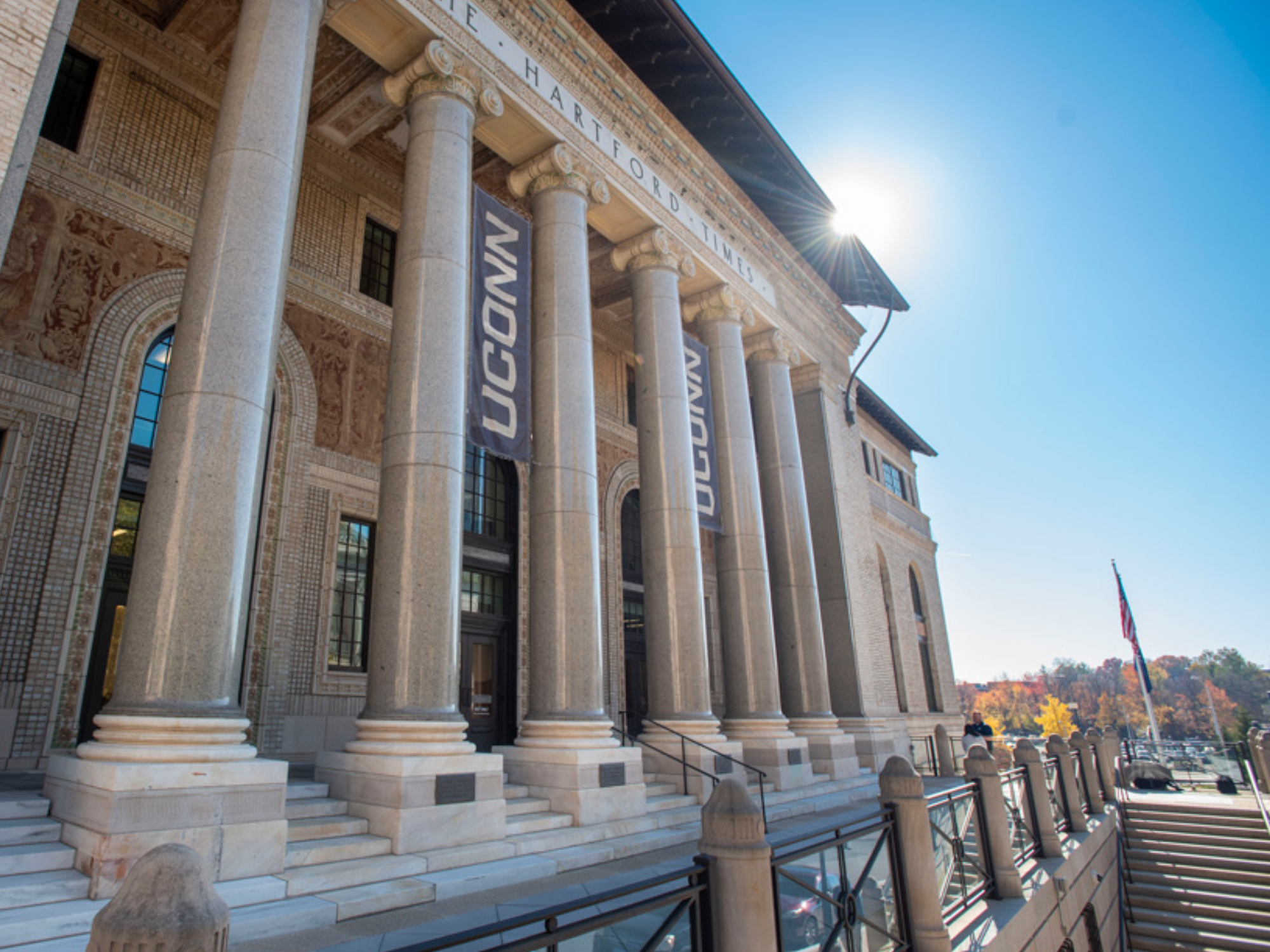 Exterior view of UConn’s Hartford campus building with tall stone columns, UConn banners, and sunlight illuminating the entrance.