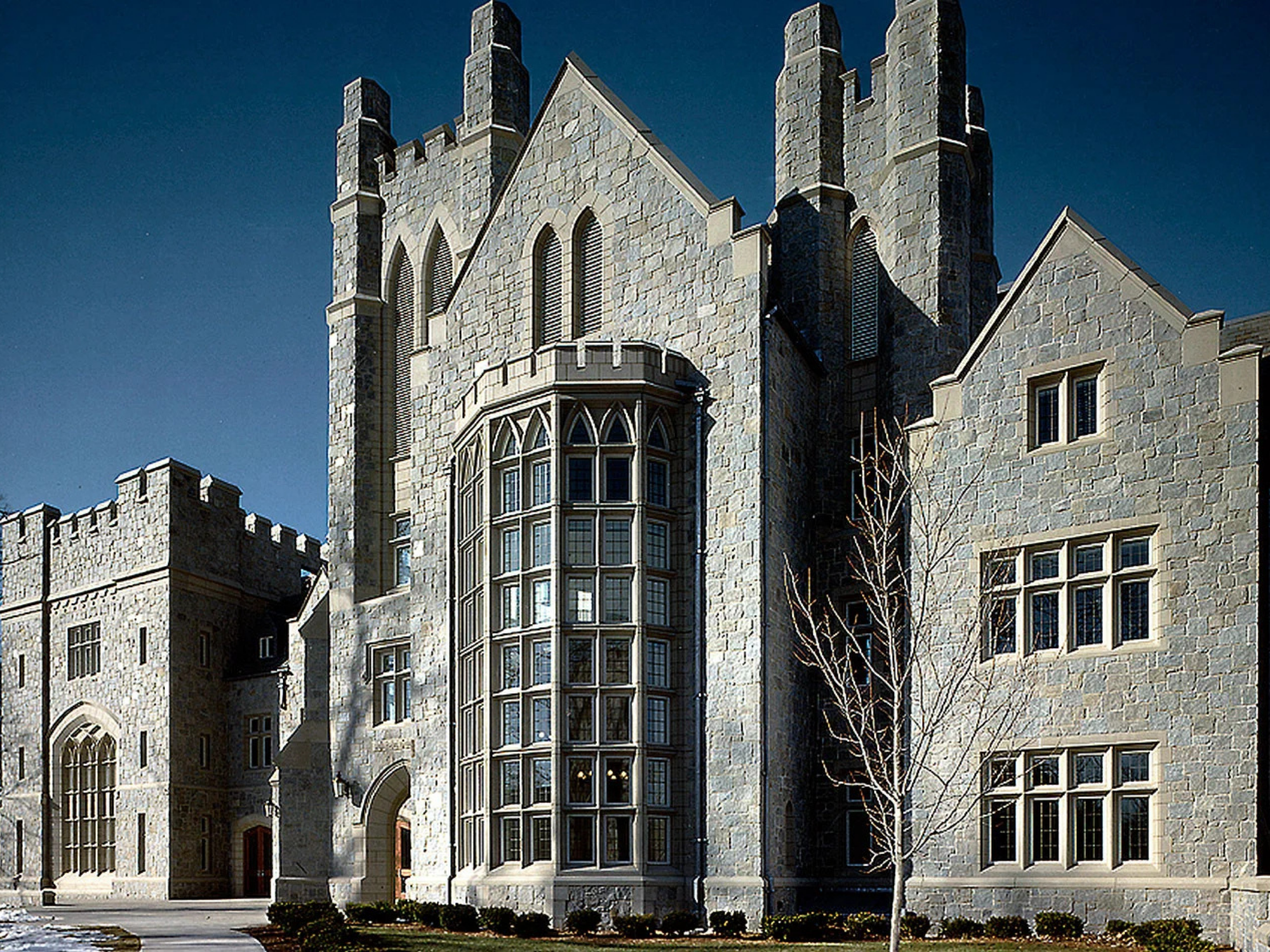 Exterior view of a historic stone campus building with Gothic-style architecture, tall windows, and castle-like towers under a clear blue sky.