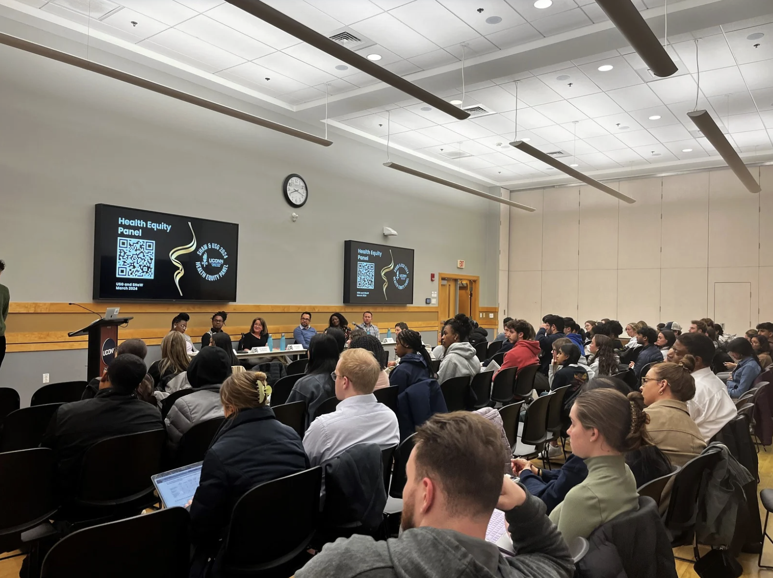 Large audience attends a UConn SHaW Health Equity panel discussion in a campus lecture hall.