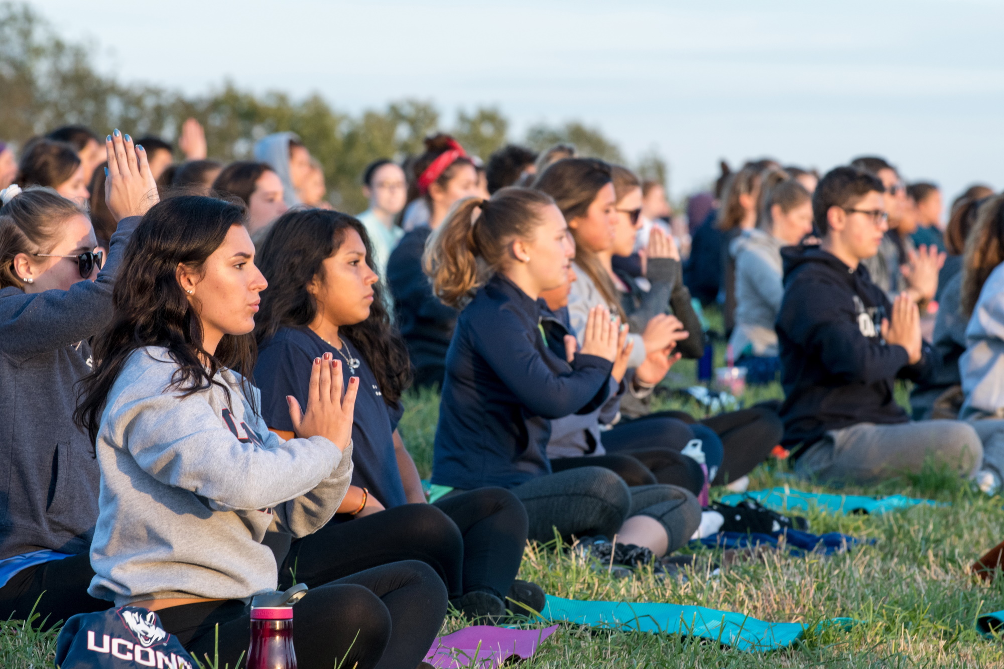 Students participate in an outdoor mindfulness and yoga session while seated on the grass at sunset.
